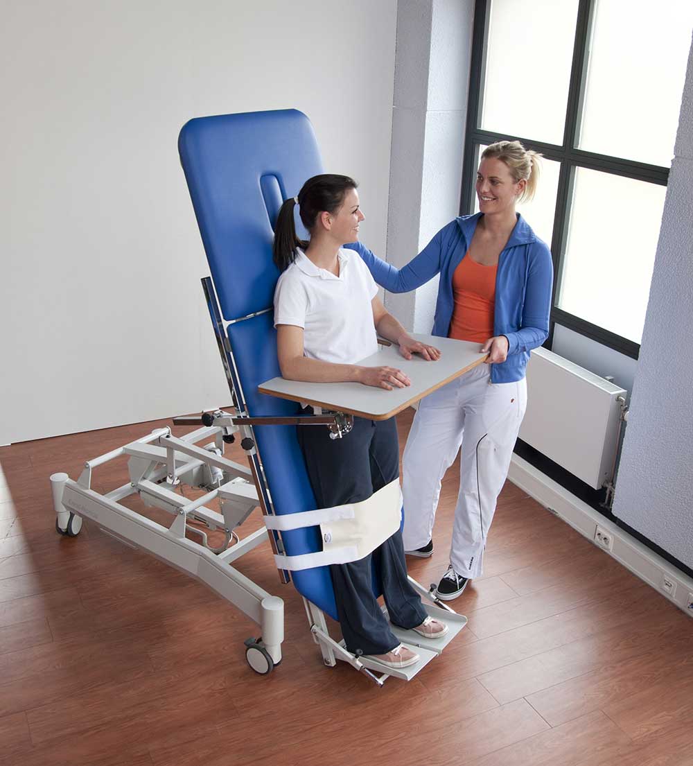 Kinésithérapeute accompagnant un patient en rééducation sur une table verticalisatrice au centre Elhatimi